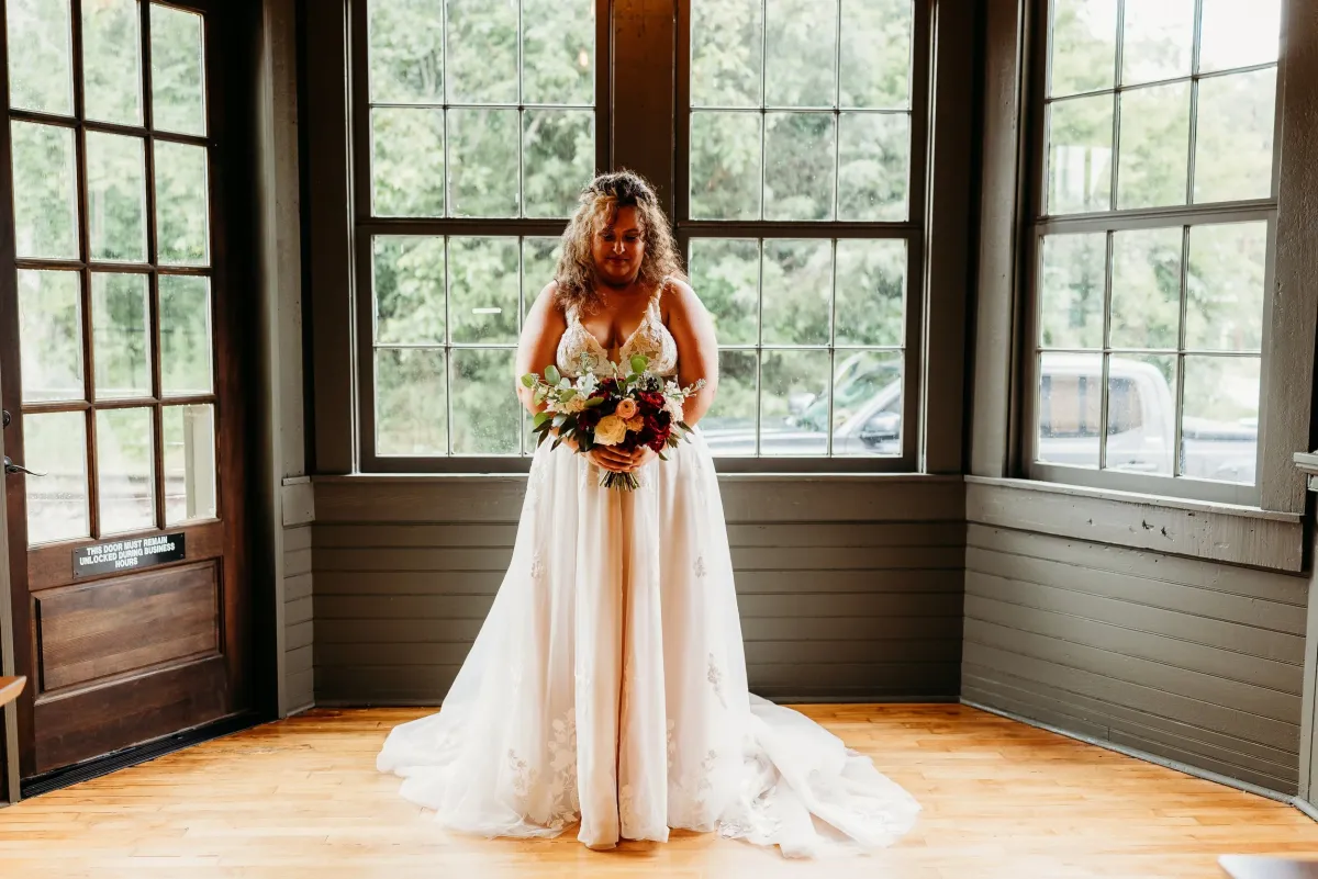 Bride holding a bold carmine bouquet in front of large windows